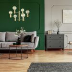 Emerald green wing back chair with pillow in grey living room interior with wooden commode